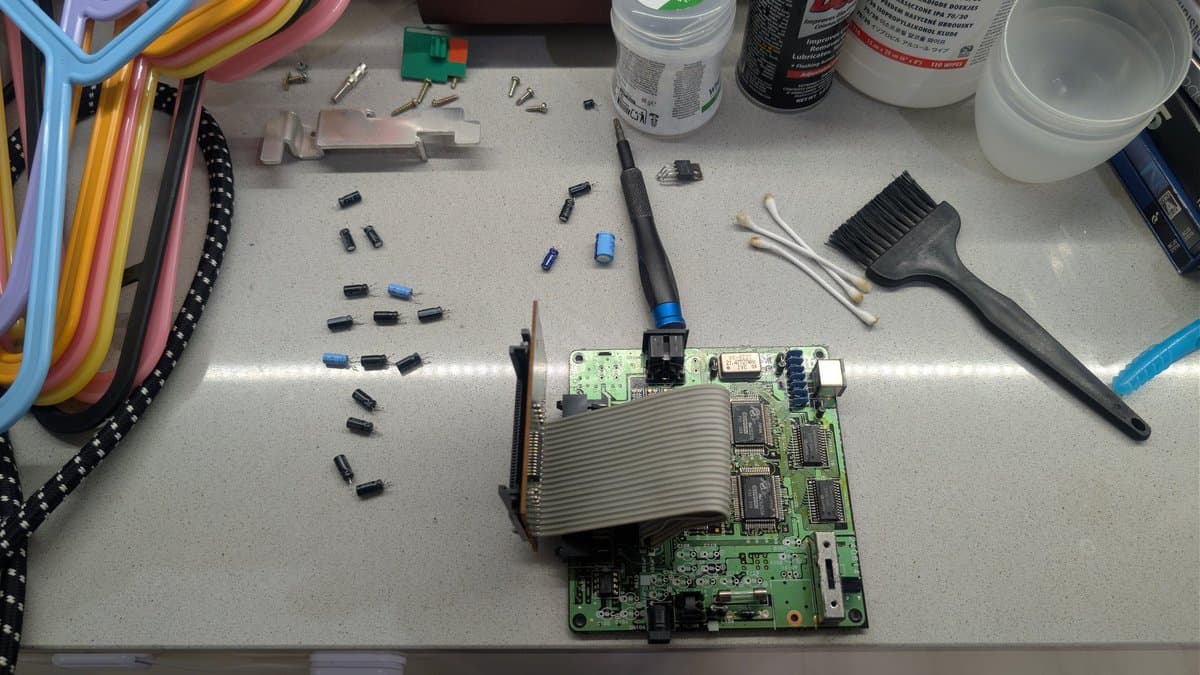 PC Engine CoreGrafx motherboard being recapped, with heatsink removed, soldering iron, capacitors, and tools visible on workbench.