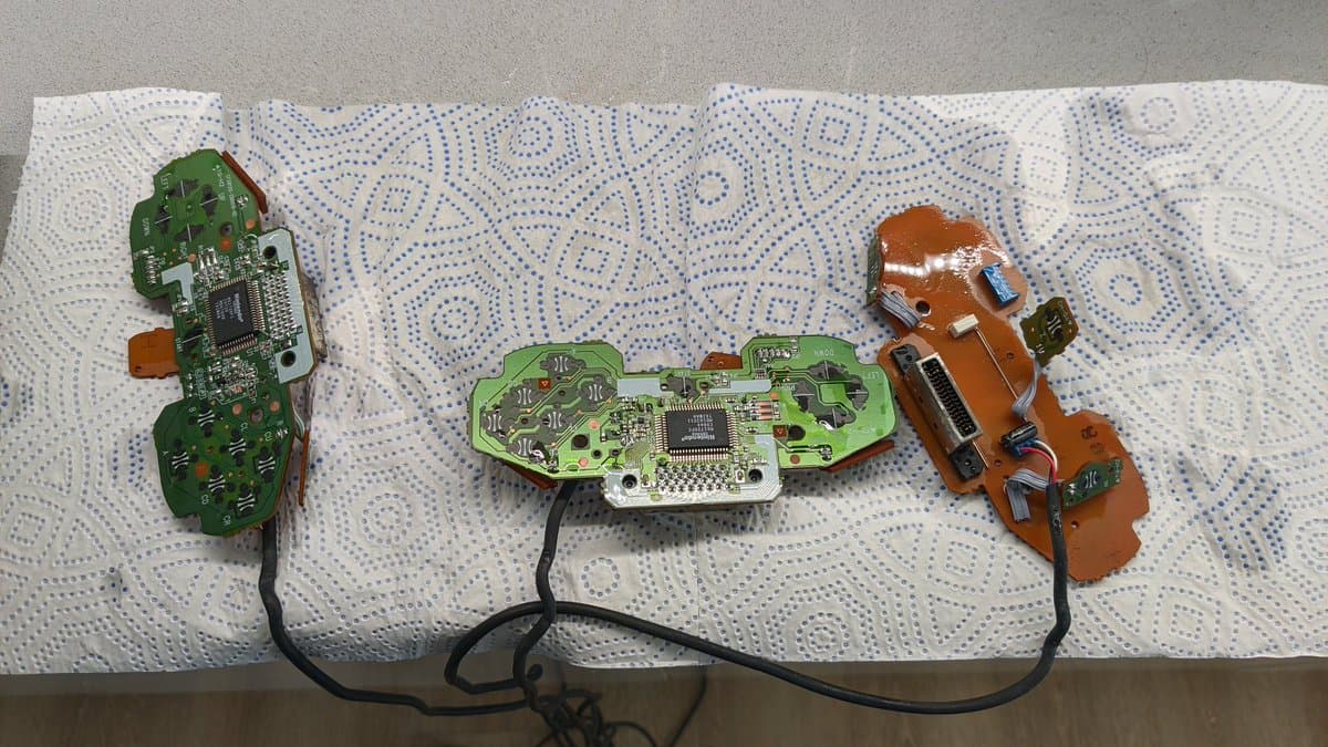 Three circuit boards from Nintendo 64 rumble packs and controllers on paper towel after ultrasonic cleaning, showing exposed PCBs with capacitors and chips.