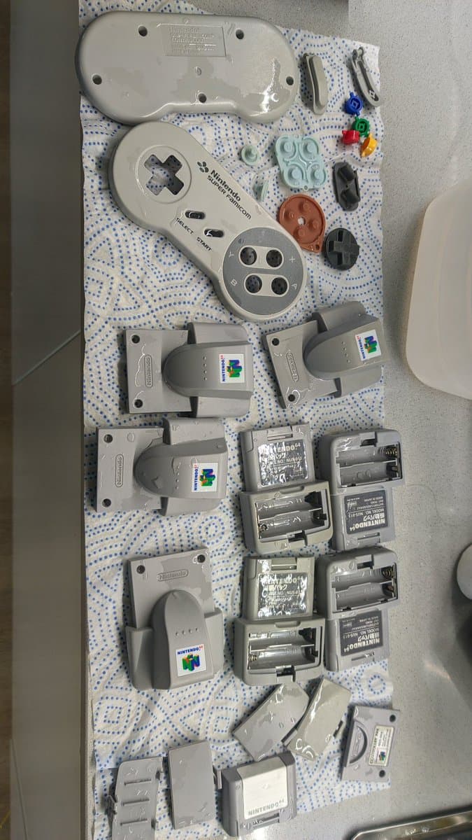 Disassembled Nintendo 64 controller parts and accessories laid out on dotted cloth after ultrasonic cleaning, including shells, circuit boards, and battery covers.