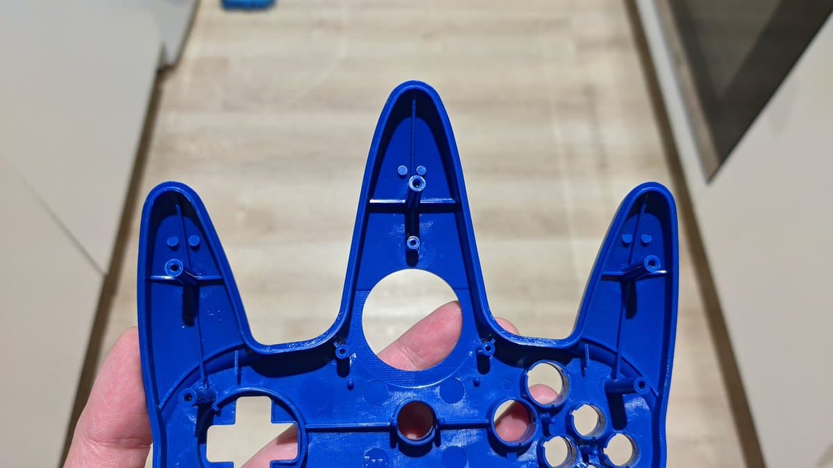 Bright blue controller shell held in hand, showing cleaned interior cavity with visible button mechanisms and mounting points after ultrasonic cleaning.