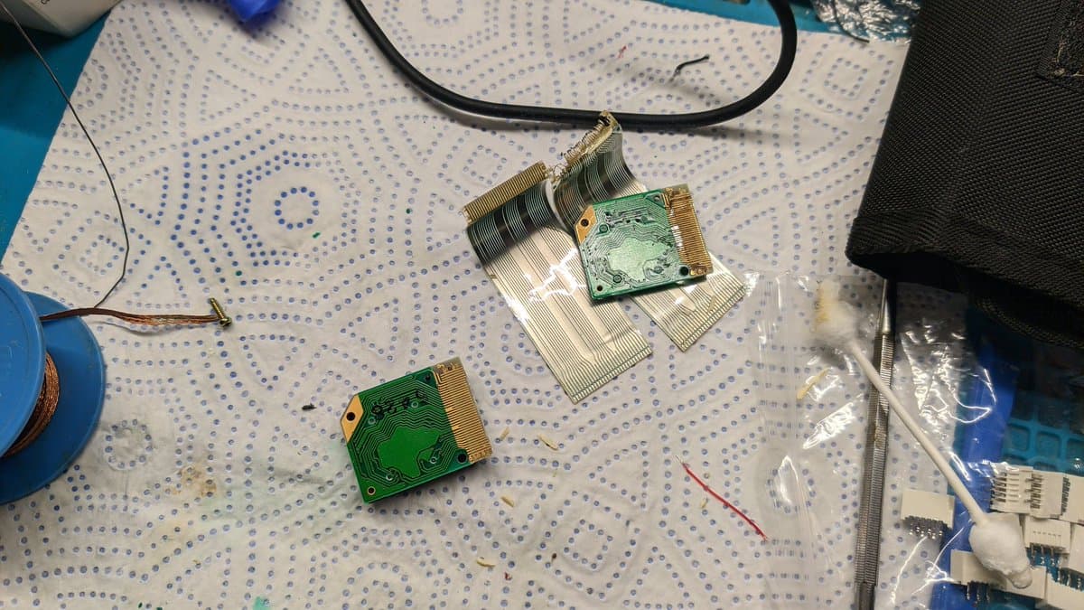 Two green LED array PCBs with flexible ribbon cables attached, one partially separated showing adhesive removal during Virtual Boy display refurbishment.