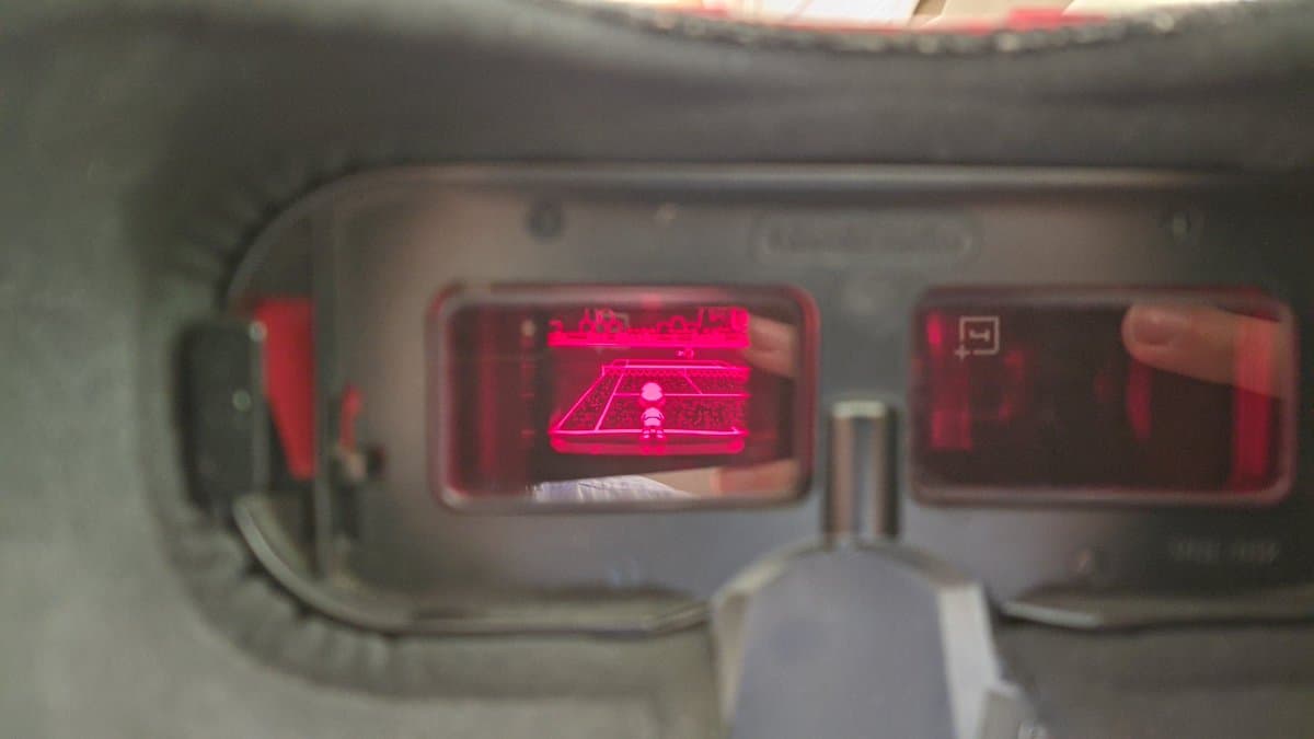 Virtual Boy display showing neon pink Pong-style game on left screen; ribbon cable installation visible through translucent housing during refurbishment.