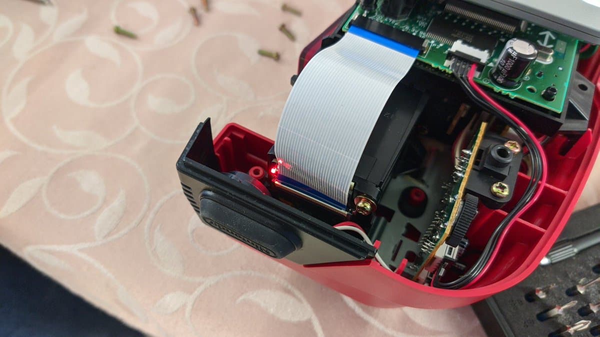 Virtual Boy internals during reassembly, showing ribbon cable installation and PCB positioning on work surface with red housing visible.