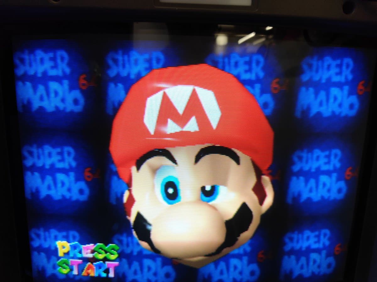 Super Mario 64 title screen on CRT displaying "SUPER MARIO" text and Mario's face, running on upgraded PicoCart64 lite flash cartridge.