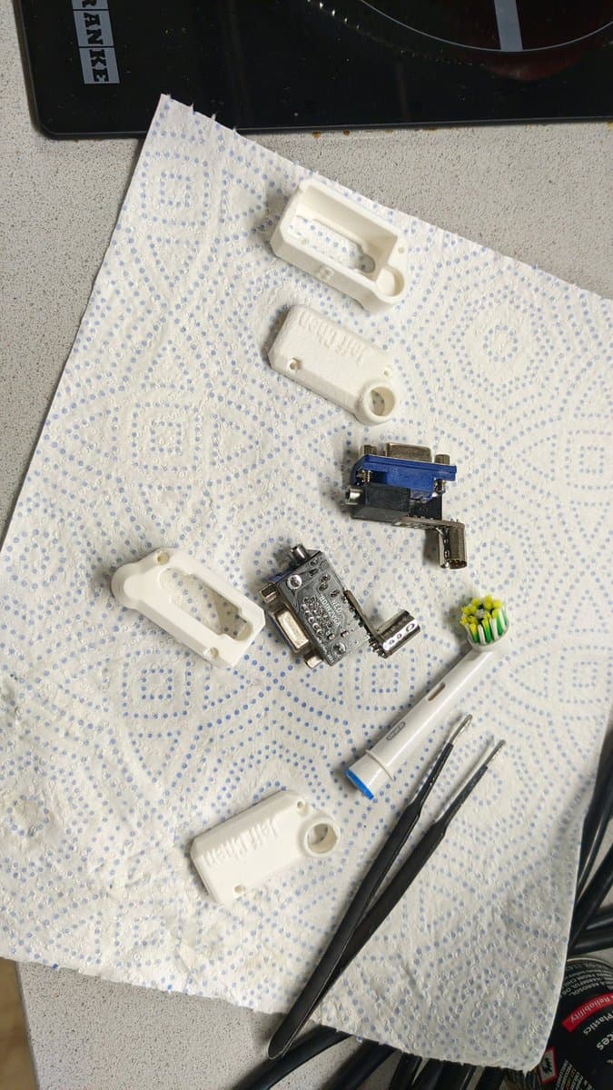 Disassembled 8DIN2VGA adapter components laid out on work mat: white plastic shells, blue PCB board, metal bracket, tools, and yellow capacitors.