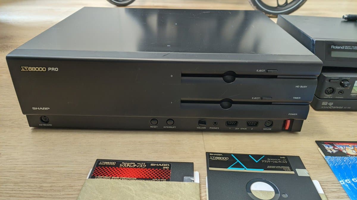 Sharp X68000 Pro II console with dual 3.5" floppy drives, front panel controls visible, alongside game disks and documentation on wooden surface.