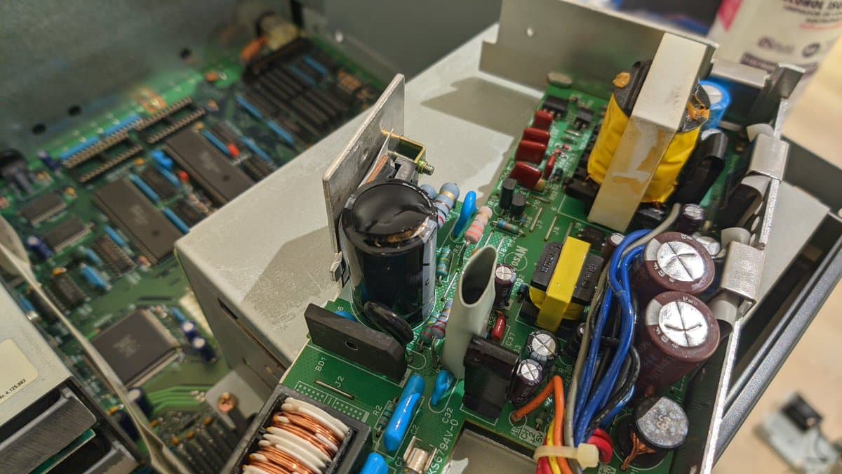 Sharp X68000 Pro II power supply board with replaced capacitors, inductor coils, and thermal damage from reversed filter installation causing component failure.