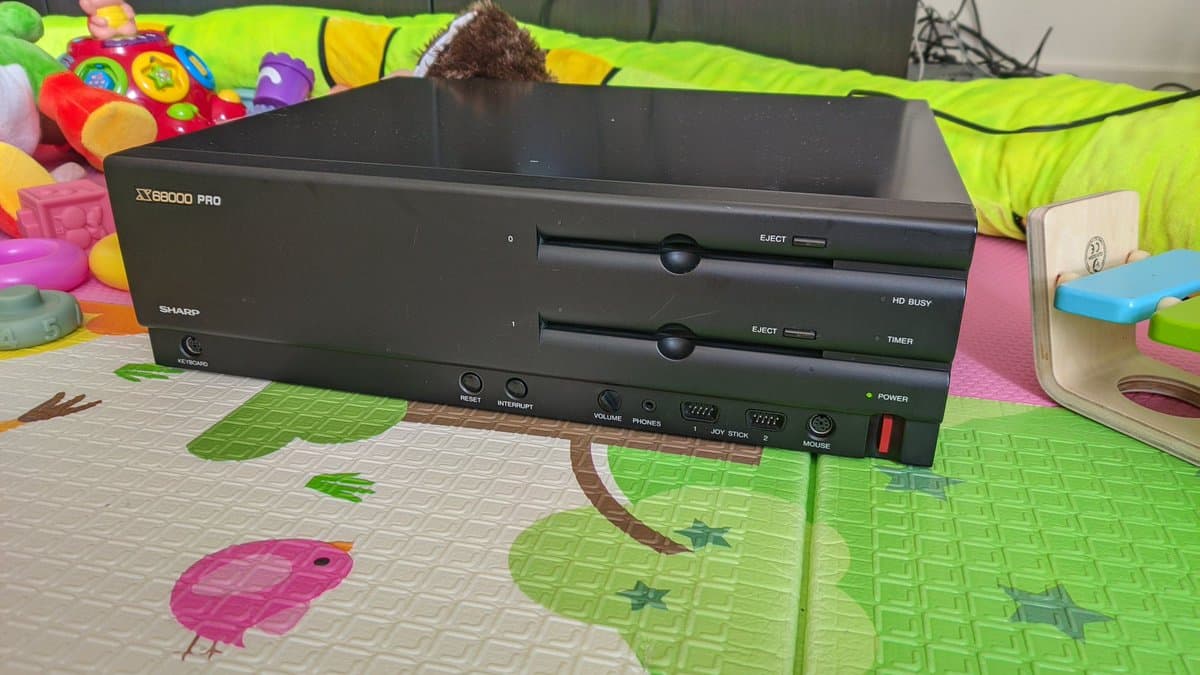 Sharp X68000 Pro II with dual disc drives displayed on colorful play mat, power LED illuminated, indicating successful boot after component replacement repair.