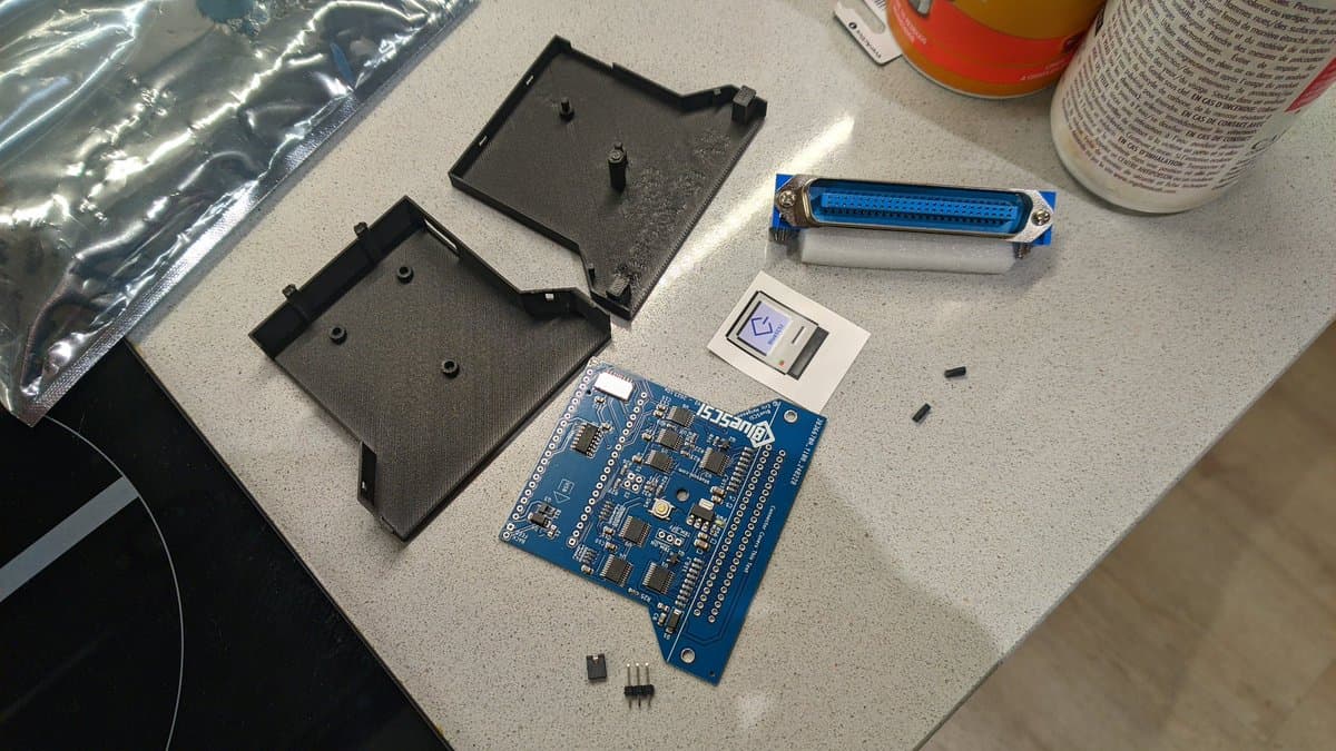 BlueSCSI v2 kit components laid out: PCB, parallel port connector, black plastic housing shells, IC chips, and small discrete components on work surface.