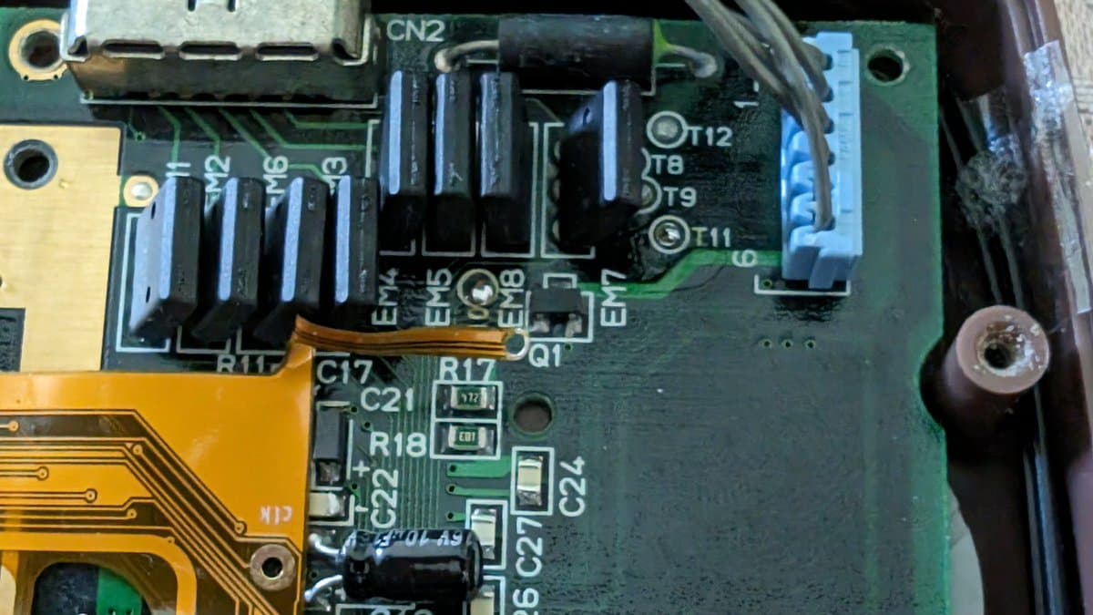 Close-up of Game Gear motherboard showing clock line bodge wire repair, capacitors, transistors, and connector CN2 with flex cable damage.
