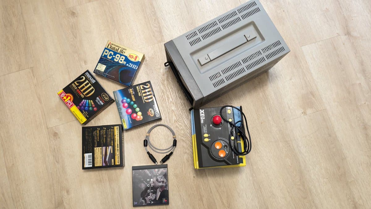 Retro gaming haul on wooden floor: Sony PVM monitor, joystick controller, PlayStation game, headphones, floppy disk boxes, and MIDI cable.