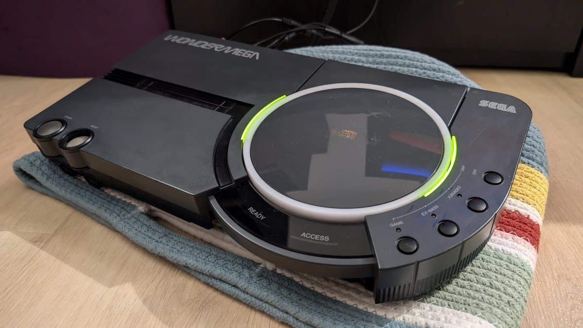 Repaired Sega Wondermega HWM-5010 display unit showing screen with green LED ring, seated on colorful cloth with cable visible.