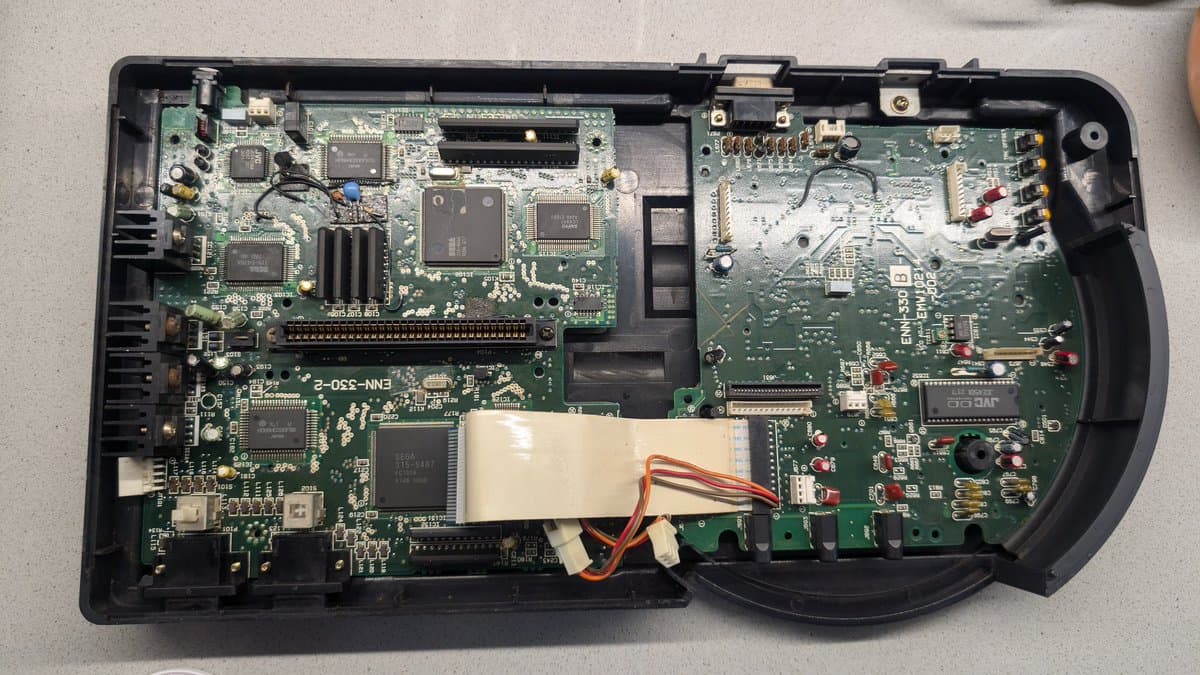 Wondermega main PCB after cleanup showing corrosion damage, faded regulator component, possible broken trace, and intact lower board section.