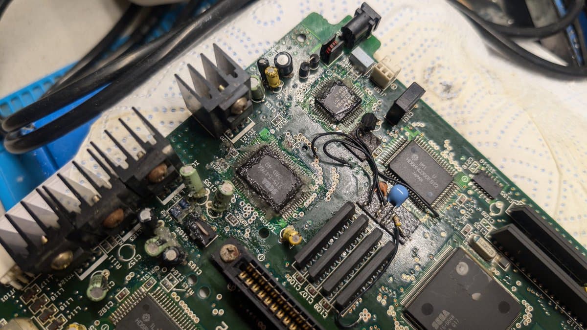 Corroded Wondermega motherboard with leaking capacitor damage, broken RAM chip legs, damaged traces, and heat sinks during restoration surgery.