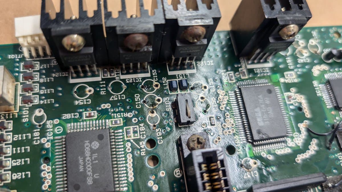 Wondermega main board with removed voltage regulators and capacitors, showing corrosion damage and exposed solder pads during restoration work.