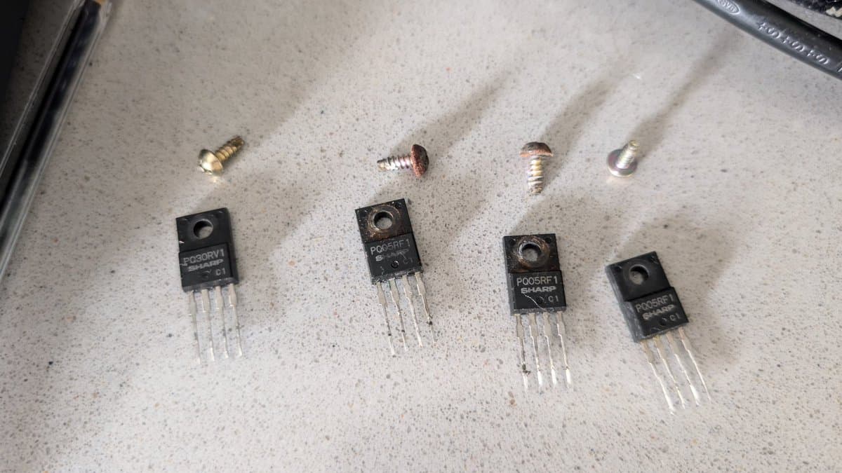 Four P065RF1 voltage regulators and four screws laid out on work surface during Wondermega capacitor and regulator removal.