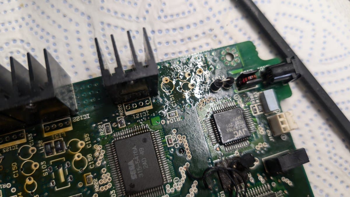 Close-up of repaired Wondermega circuit board showing new solder joints, replaced components, and a black heat sink on breadboard.