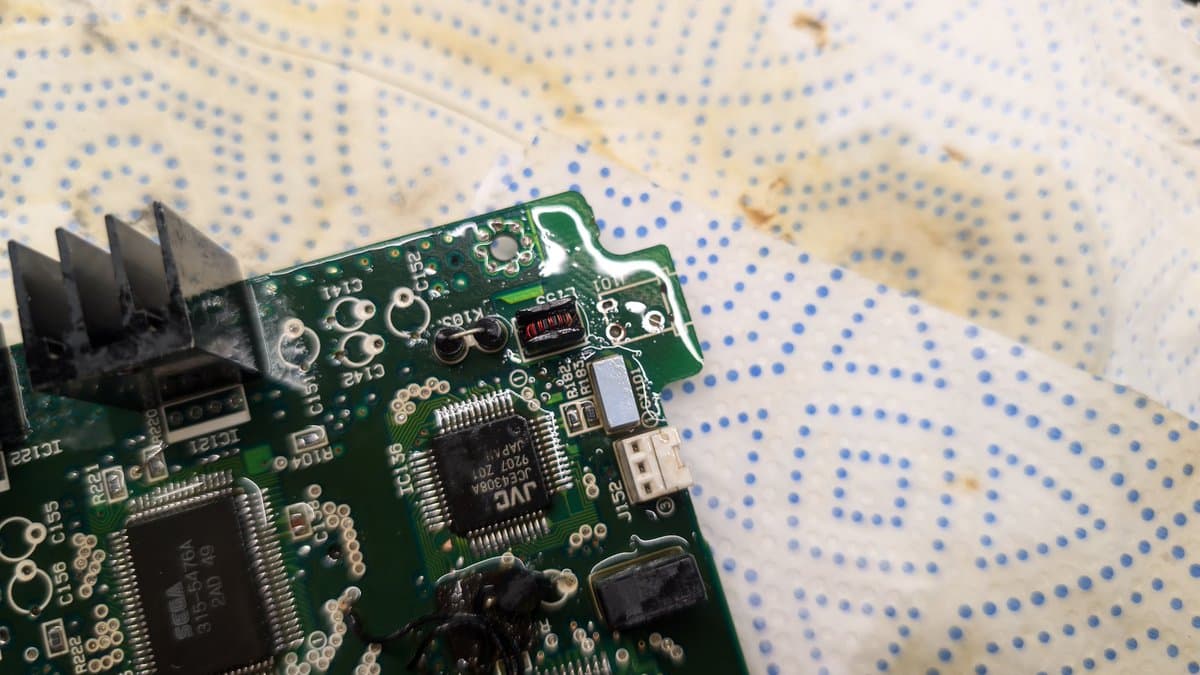 Sega Wondermega PCB with removed power jack showing corroded through-holes and component pads needing Deoxit treatment.