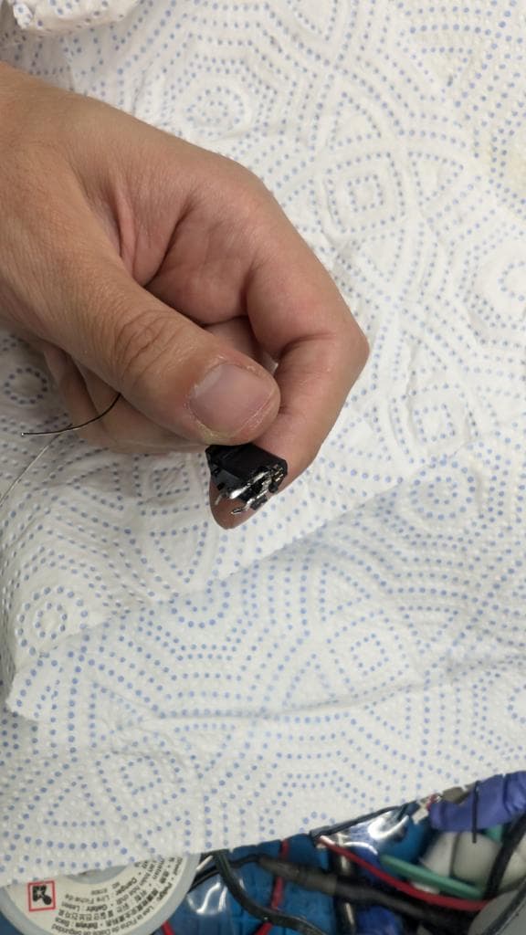 Close-up of tinned regulator legs being held with tweezers over patterned fabric during Wondermega restoration work.