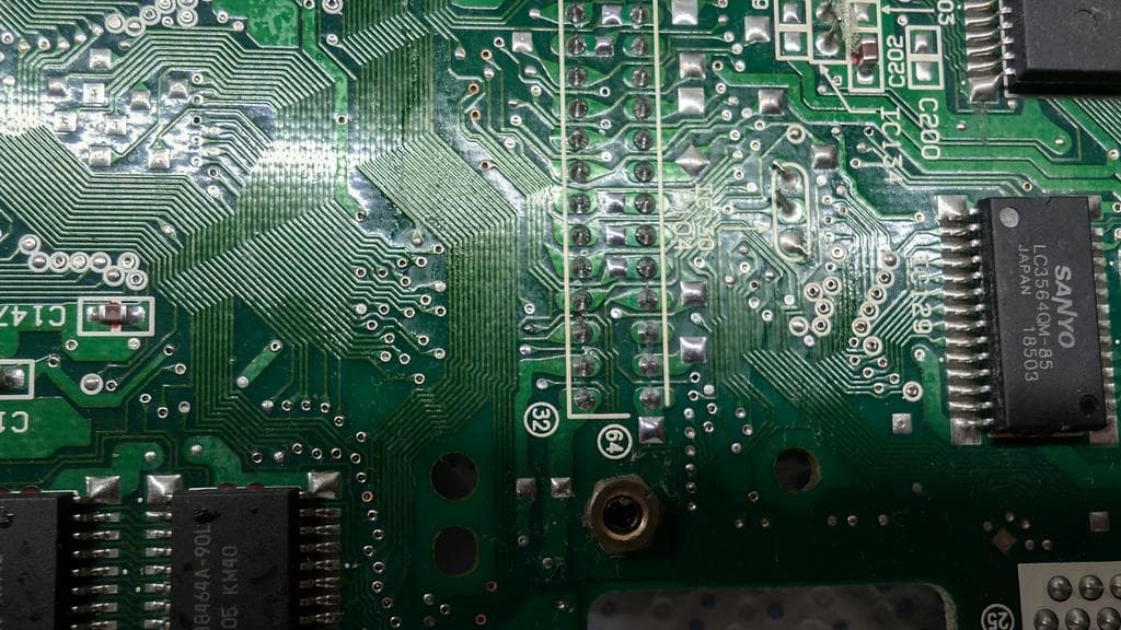 Wondermega circuit board close-up showing corroded traces, solder joints, and IC chips including Sega processor. Damage visible on green PCB.