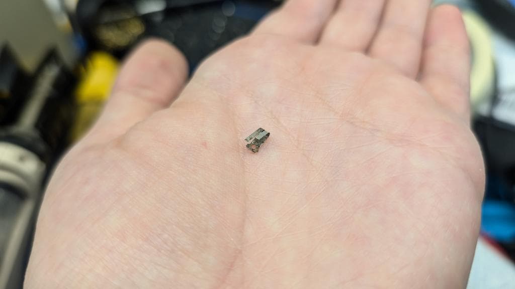 Small electronic component held in palm of hand during Wondermega repair, showing scale of tiny circuitry work.