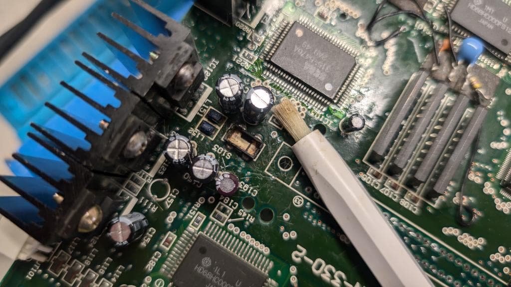 Wondermega circuit board after cleaning, showing reassembled power button area with visible capacitors, IC chips, and cleaned cartridge slot contacts on top side.