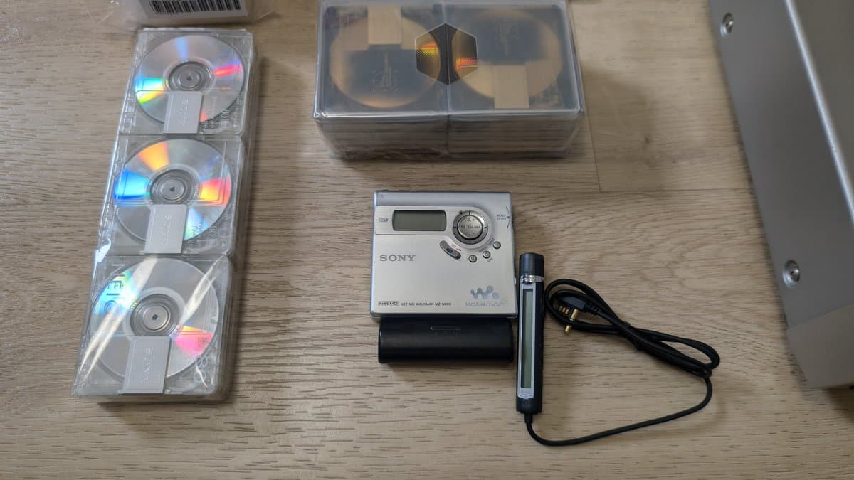 Sony MiniDisc portable player MZ-N920 with three MD discs, remote control, and battery pack displayed on wooden surface.