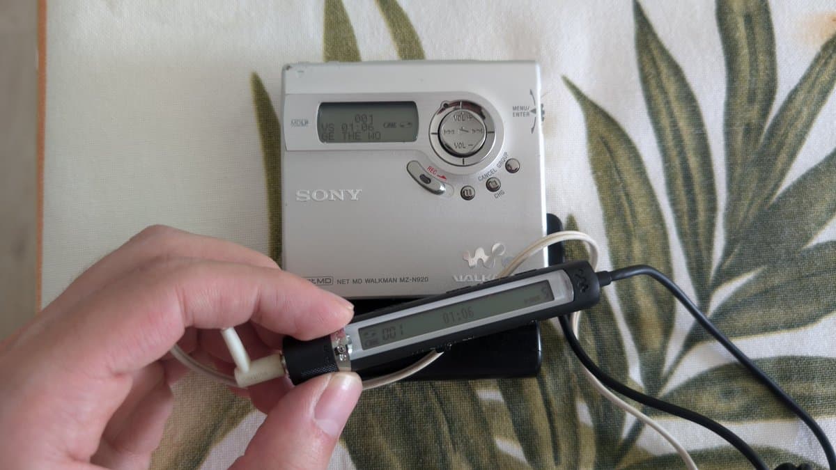 Hand holding Sony MZ-N920 MiniDisc Walkman with remote controller displaying LCD screen, device in working condition.