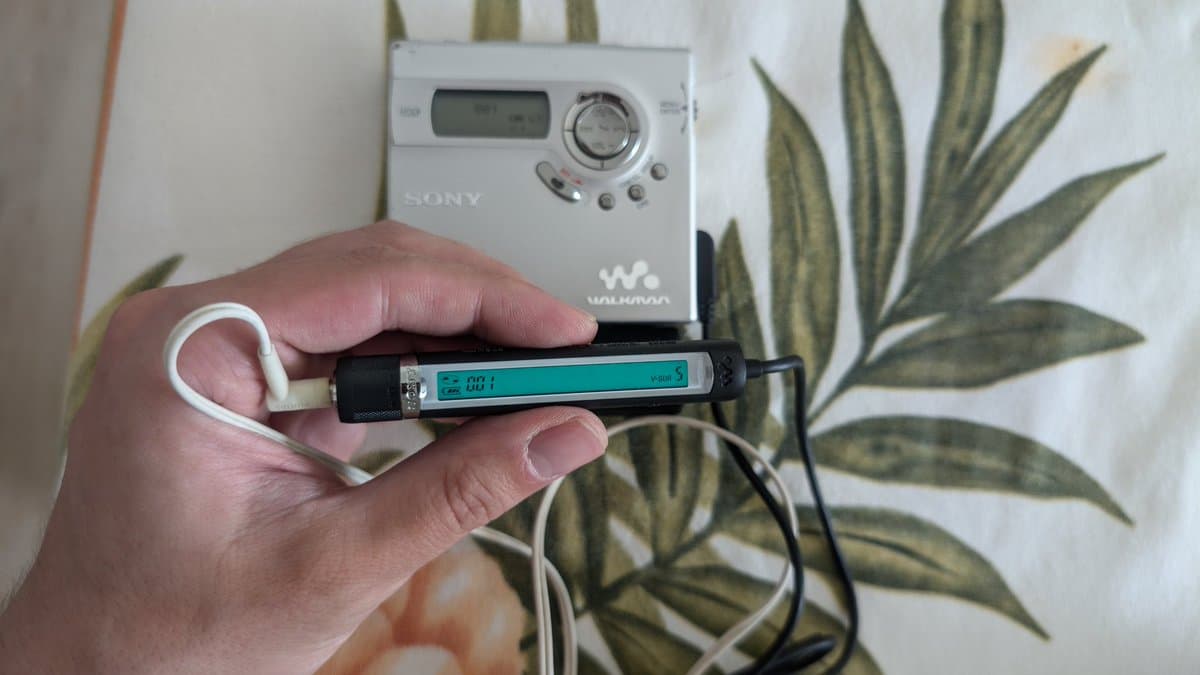 Hand holding Sony MiniDisc remote controller with turquoise LCD display showing 88.1 FM, MZ-N920 portable player visible in background.