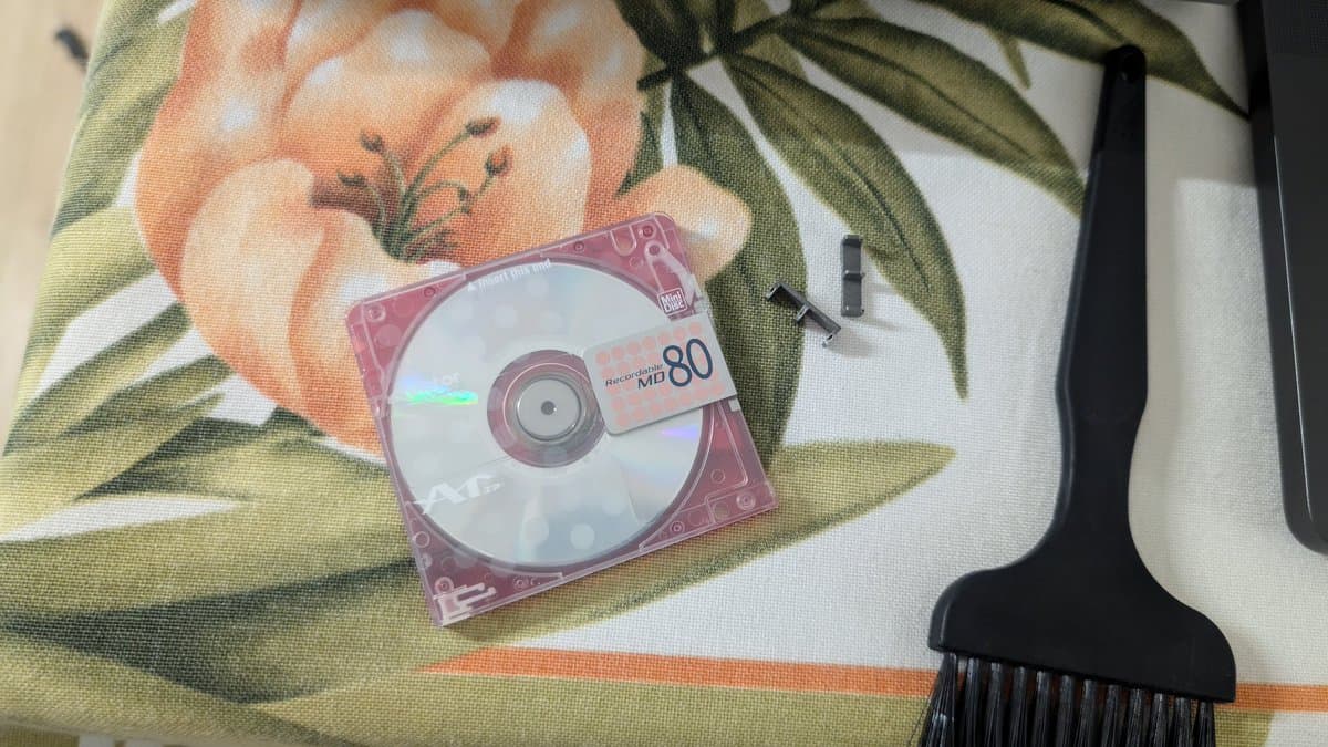 Pink Sony MDS-S500 MiniDisc deck with MD80 disc on floral fabric, black brush tool visible at right edge.