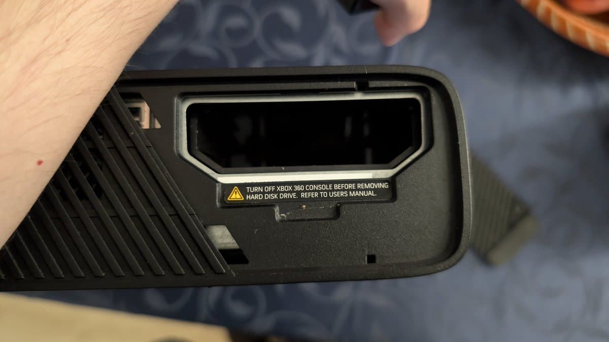 Xbox 360 E hard drive bay with warning label visible, empty drive slot ready for HDD installation after recap and reflow repair.