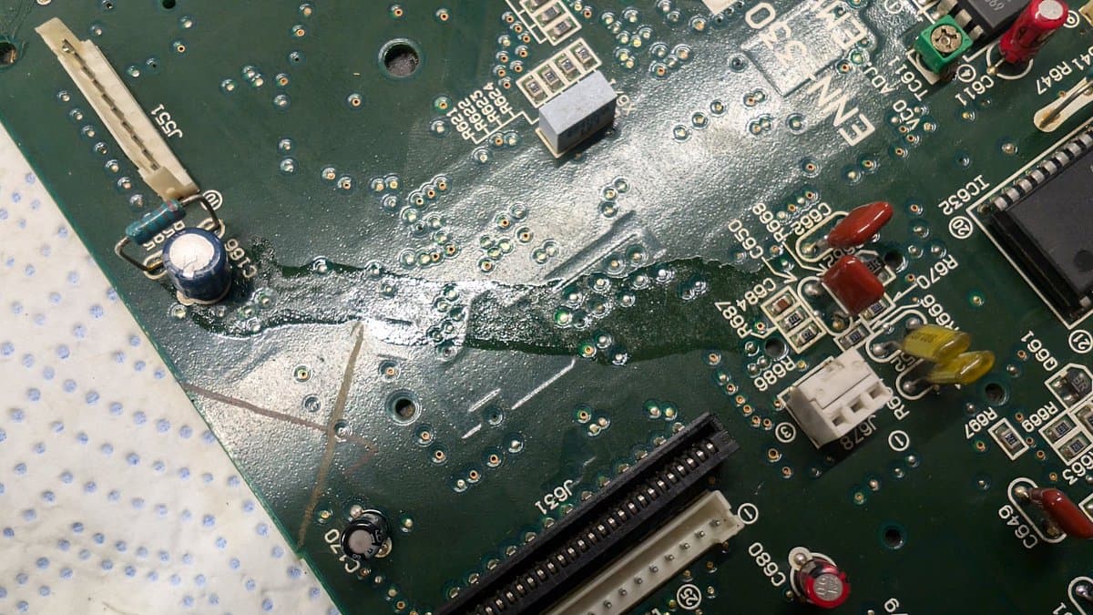 Wondermega circuit board during capacitor replacement surgery; visible sludge residue, desoldered caps, and corroded traces from previous damage.