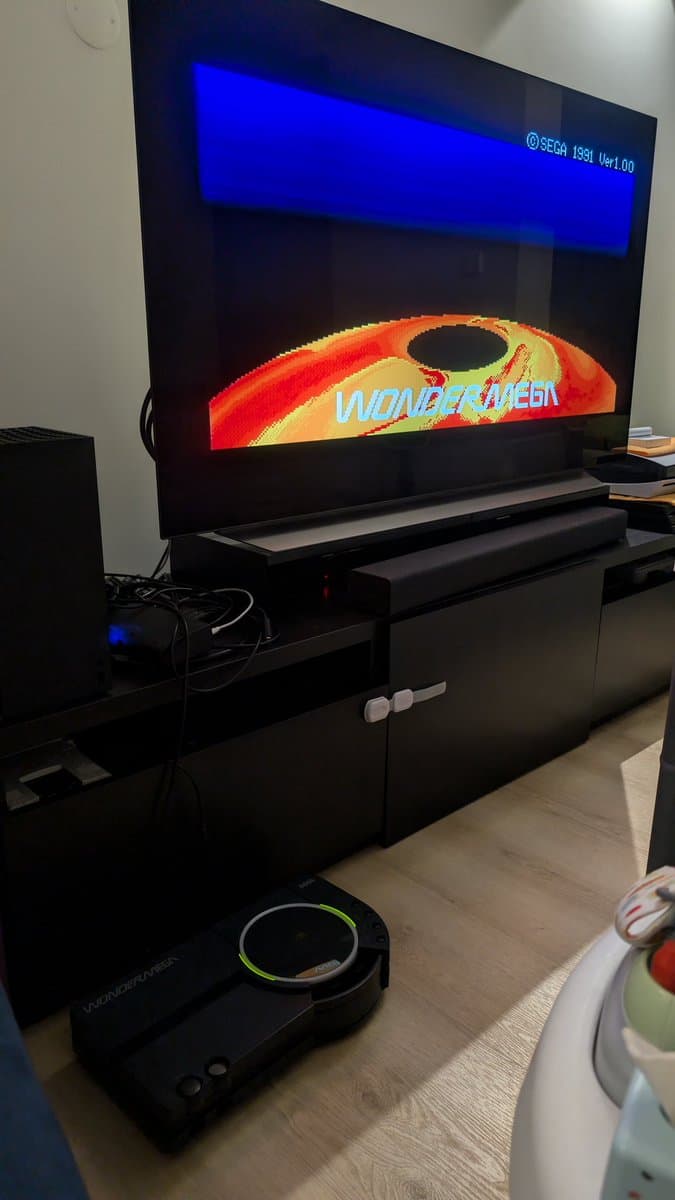 Sega Wondermega displaying title screen with freeze issue; console on black stand with controller below, repair still in progress.