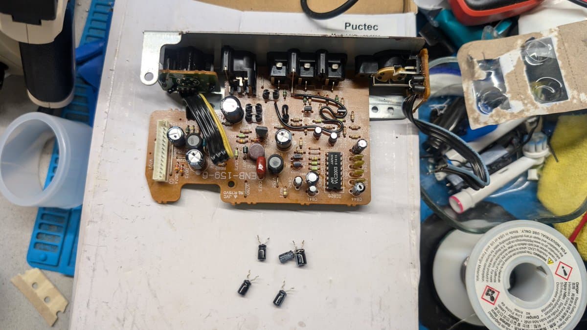Sega Wondermega AV board with removed electrolytic capacitors displayed below, showing corroded PCB and components requiring replacement during restoration.