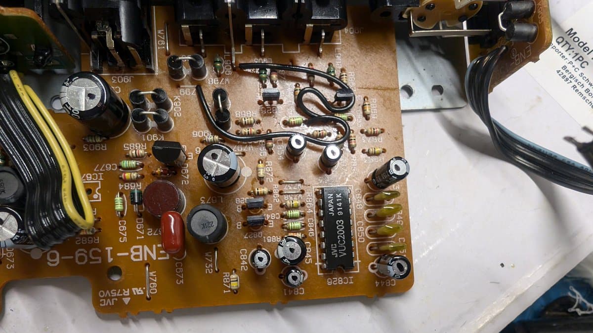 Sega Wondermega AV board PCB with multiple capacitors being replaced; electrolytic capacitors and resistors visible among circuit traces and solder joints.