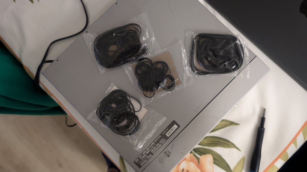 Four replacement belts in clear plastic packaging arranged on white surface with repair documentation and stylus nearby.