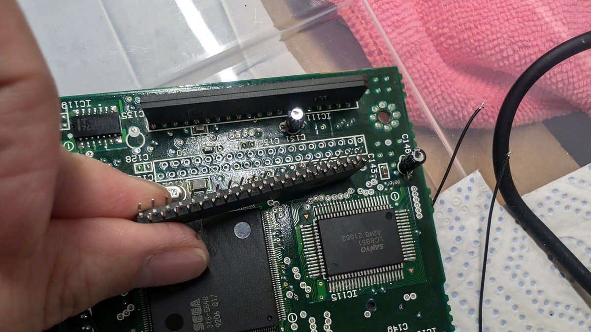 Close-up of Wondermega circuit board showing desoldered RAM package being inspected for broken legs during repair work.