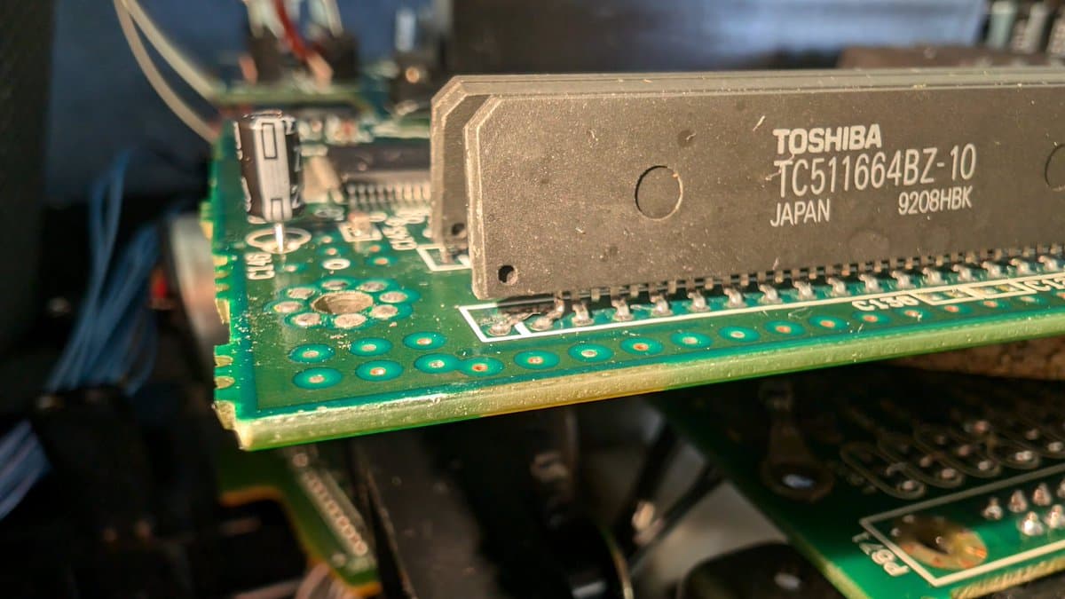 Close-up of Toshiba TC511664BZ-10 RAM chip with visibly broken legs on green PCB during Wondermega voltage diagnostics.