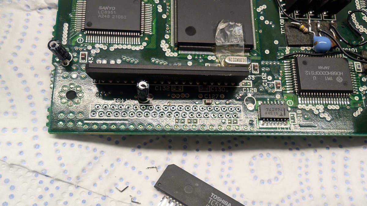 Extracted RAM chip with three broken legs displayed below Wondermega motherboard during repair documentation.