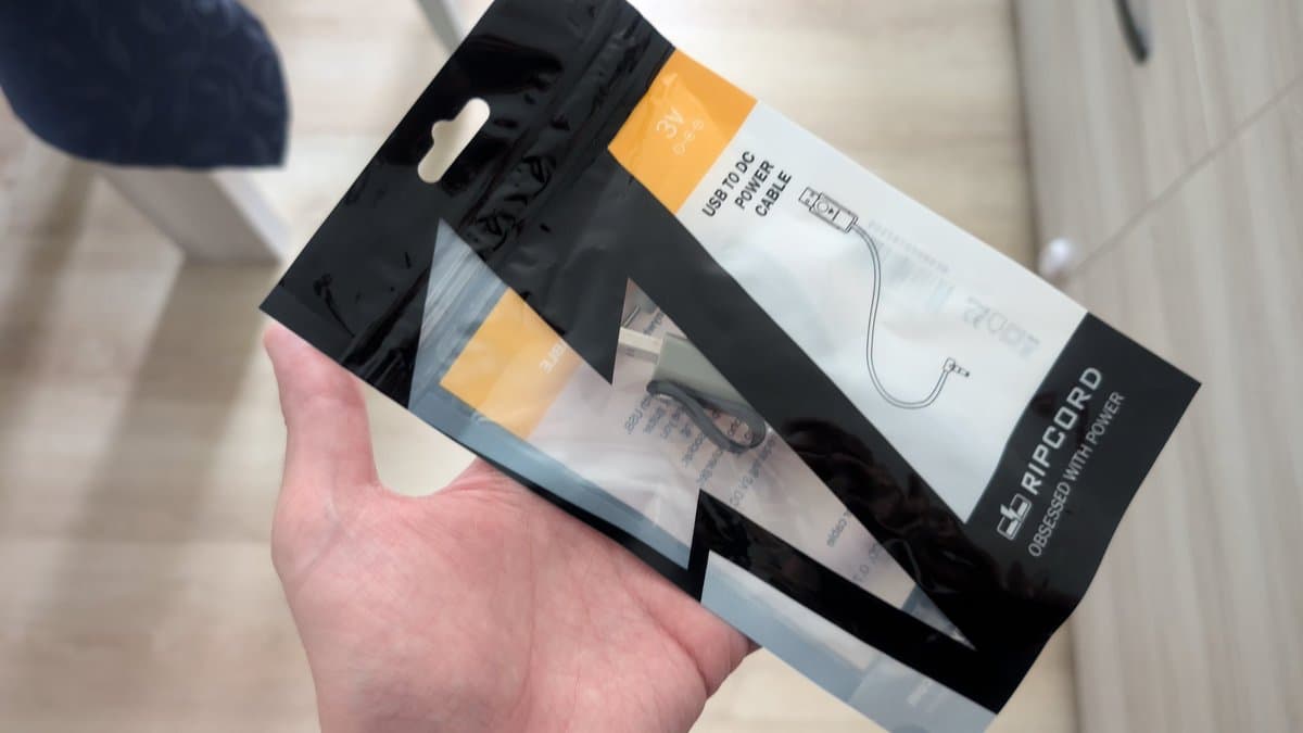 Hand holding MiniDisc charging cable package with USB power adapter and cord visible through clear packaging window.