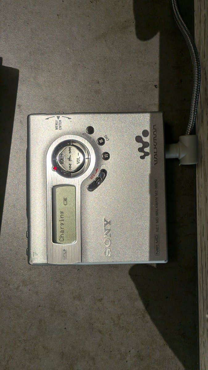 Sony MZ-N920 portable MiniDisc player with charging cable connected, displaying battery indicator on LCD screen.