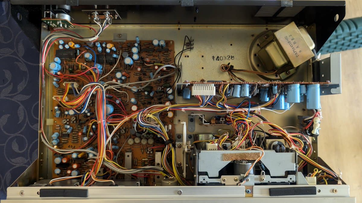 Interior of Victor KD-A6 cassette deck powered on, showing multiple blue capacitors, circuit boards, wiring harness, and transformer requiring capacitor replacement.