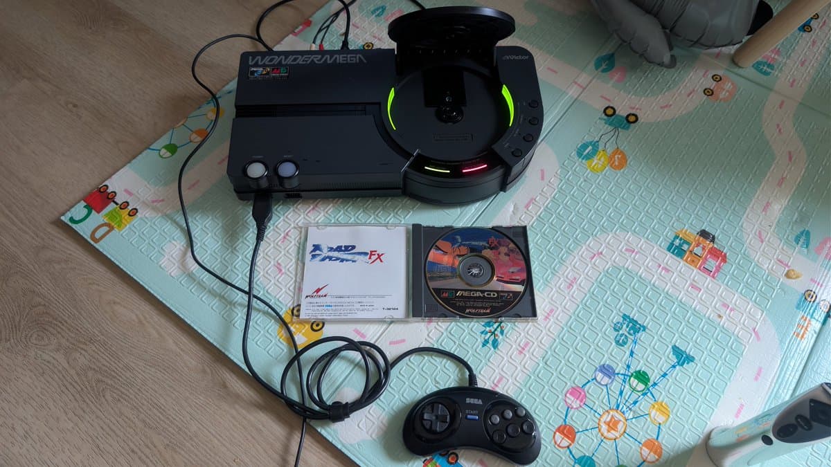 Restored Sega Wondermega with green LED indicators lit, displayed with test games Road Avengers and Dynamite Headdy, Sega controller, and cables on work mat.