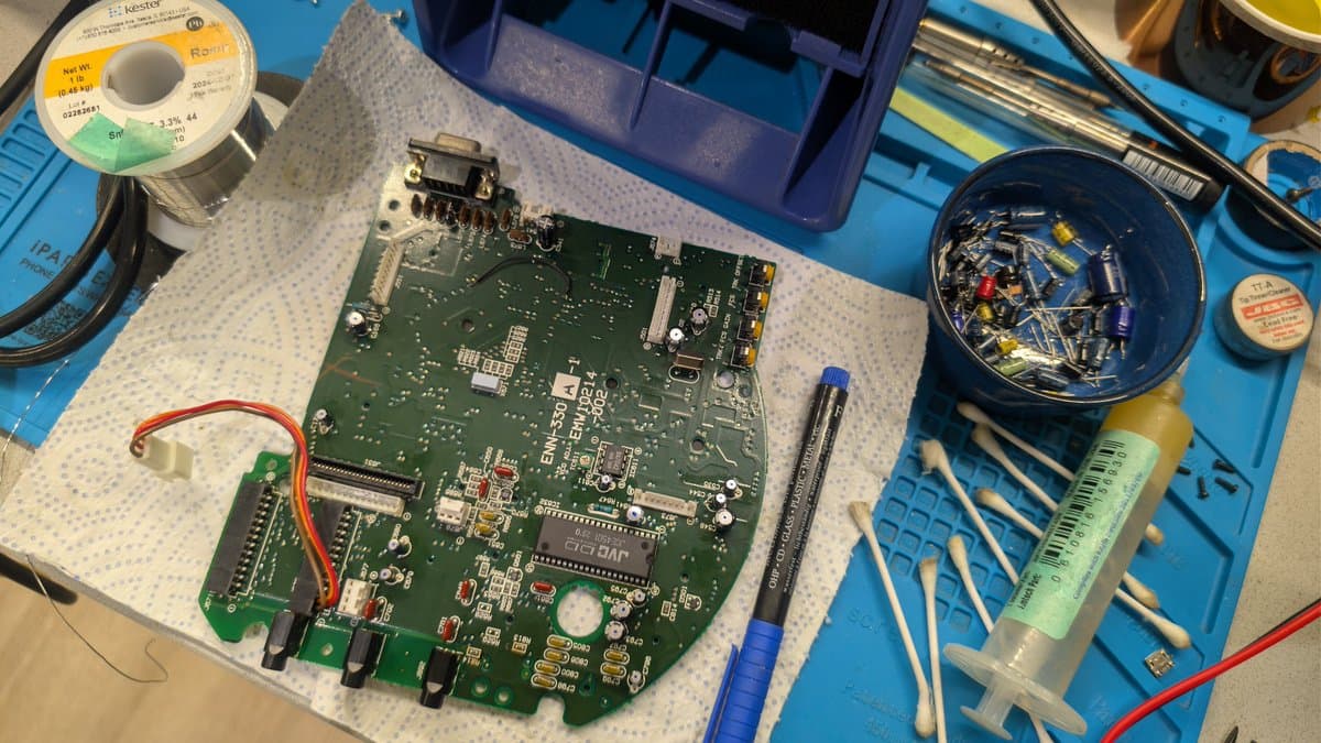 Victor RG-M1 AV board during recap with soldering iron, capacitors in blue bowl, solder spool, and antistatic mat on work surface.