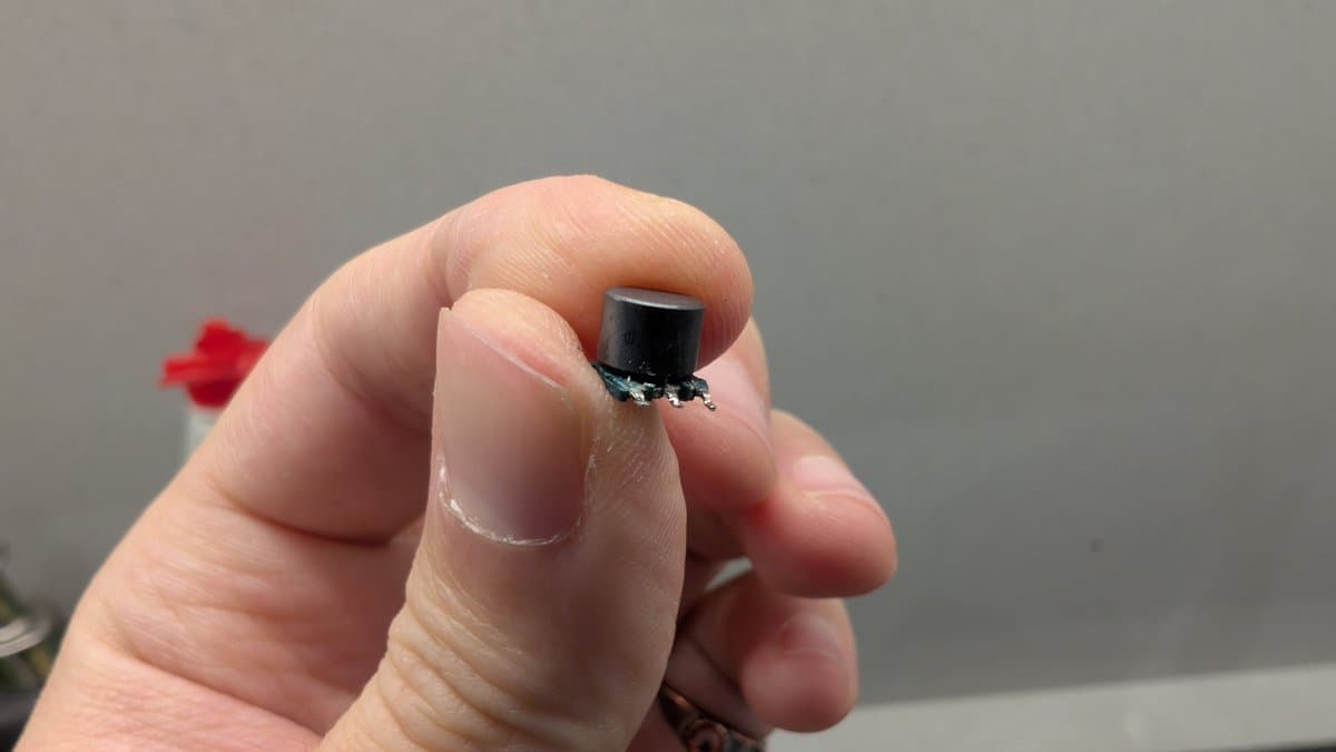 Close-up of a finger holding a tiny black component (T500 transformer) with a visibly broken wire on its output side from NEC PC Engine LT LCD repair.