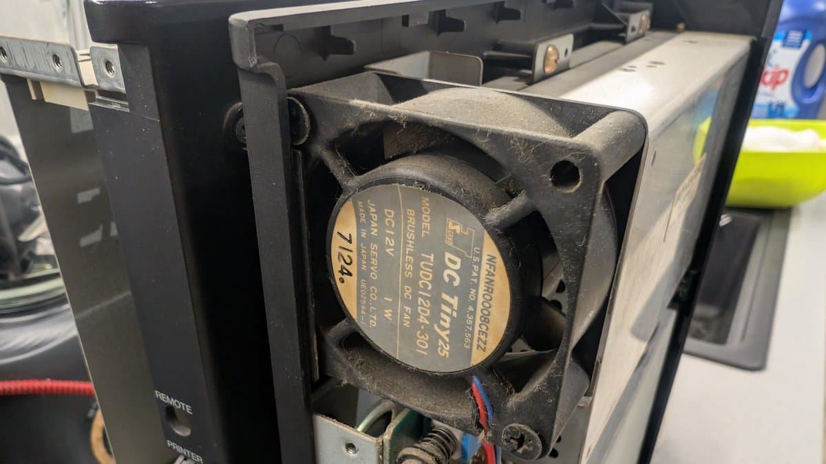Close-up of DC fan with tan label inside Sharp X68000 chassis, showing cooling unit mounted in black plastic housing with wiring.