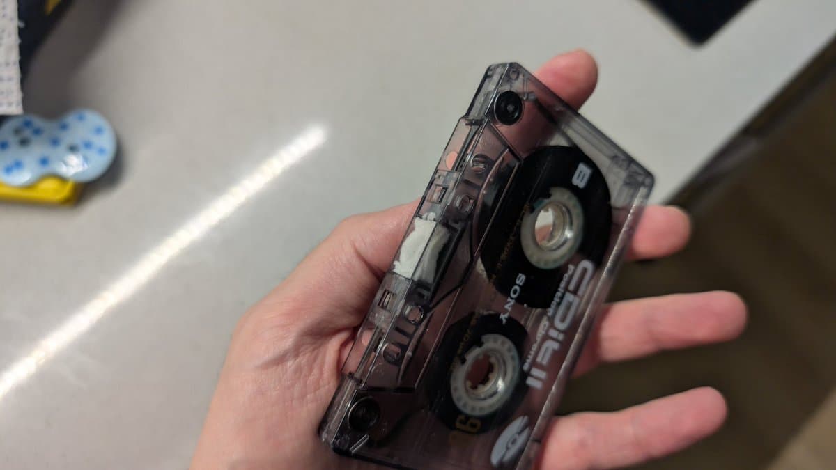 Hand holding transparent cassette tape showing dual reels and internal mechanisms with visible tape spools and metal components.