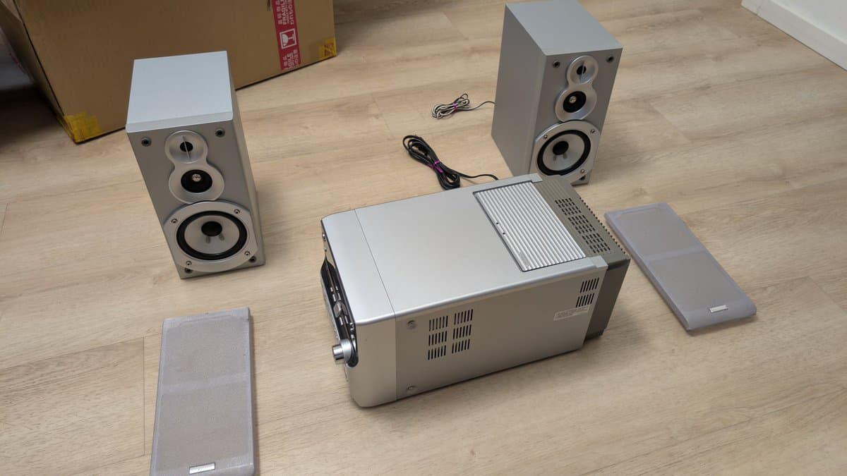 Victor stereo system with cassette, MiniDisc, and CD player surrounded by two speakers and accessories on wooden floor.