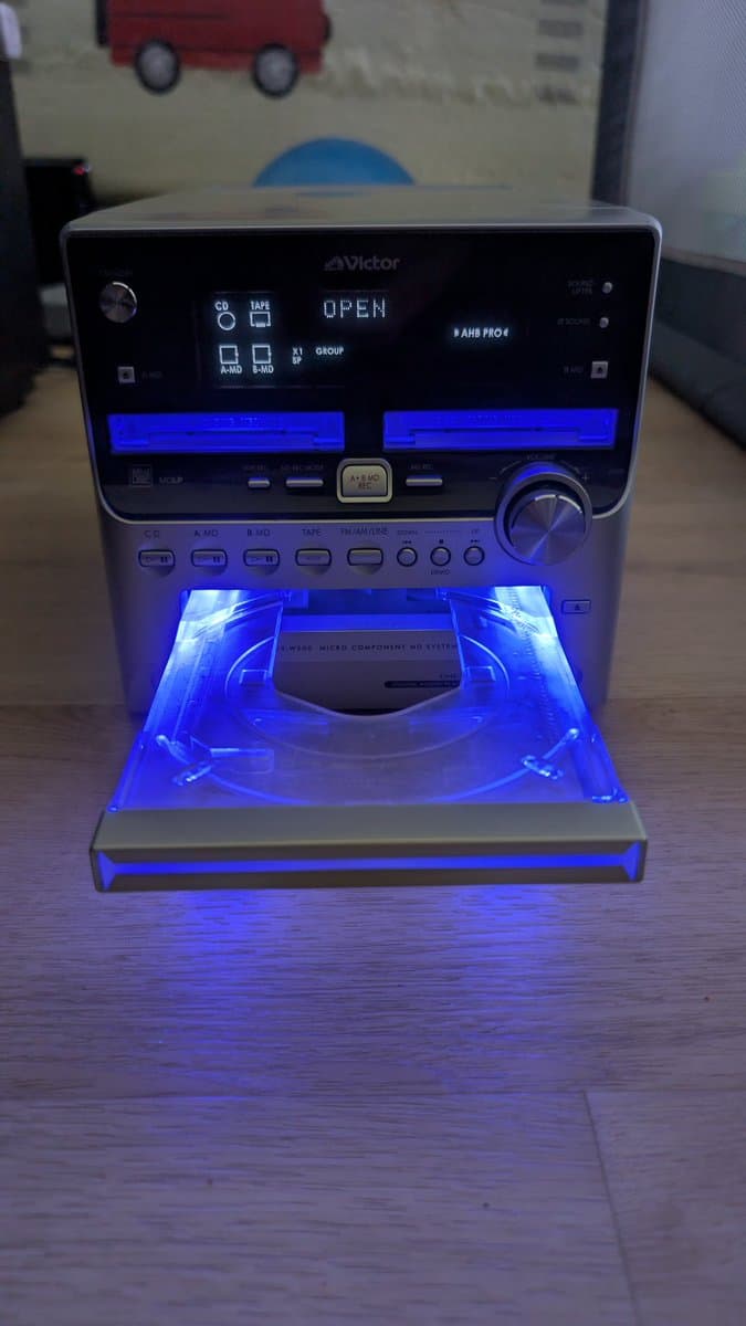 Victor stereo system with open disc tray illuminated by blue LED, displaying disc mechanism and loading components during MiniDisc repair work.