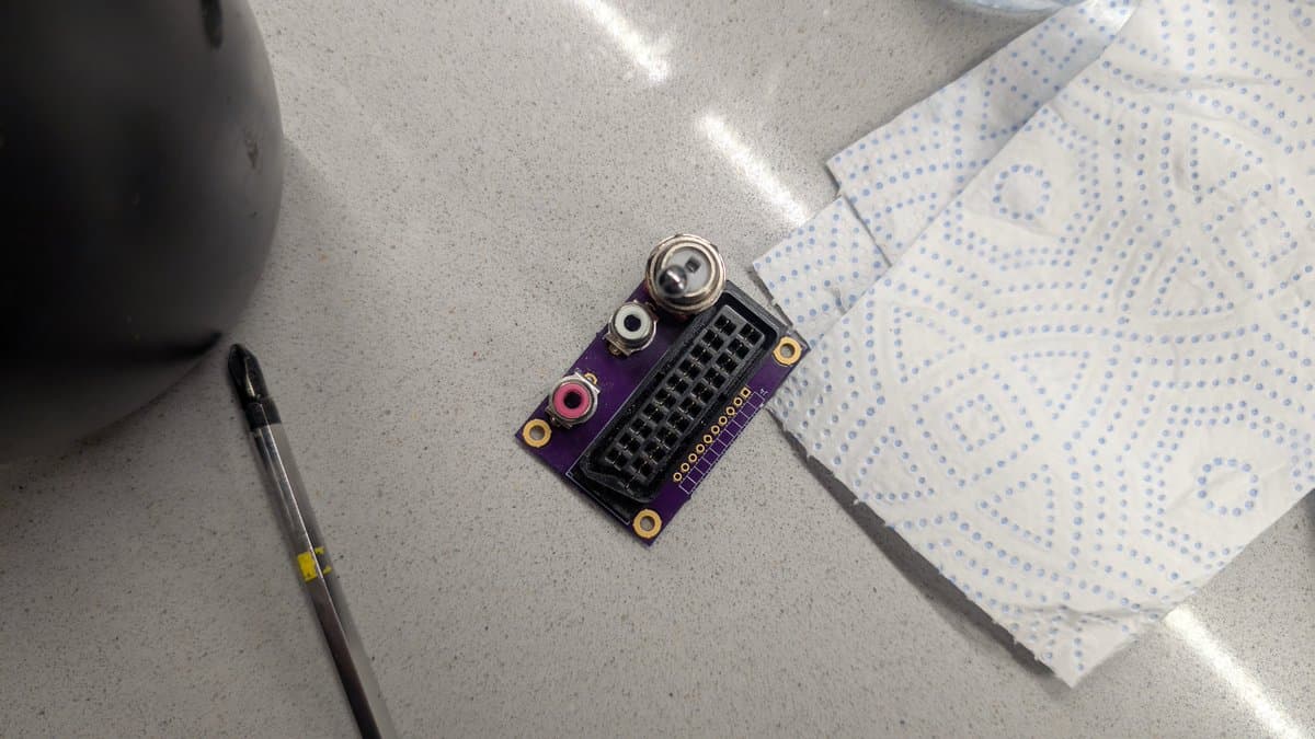 RGB mod PCB assembly on concrete surface next to breadboard and screwdriver, showing connectors and solder joints.